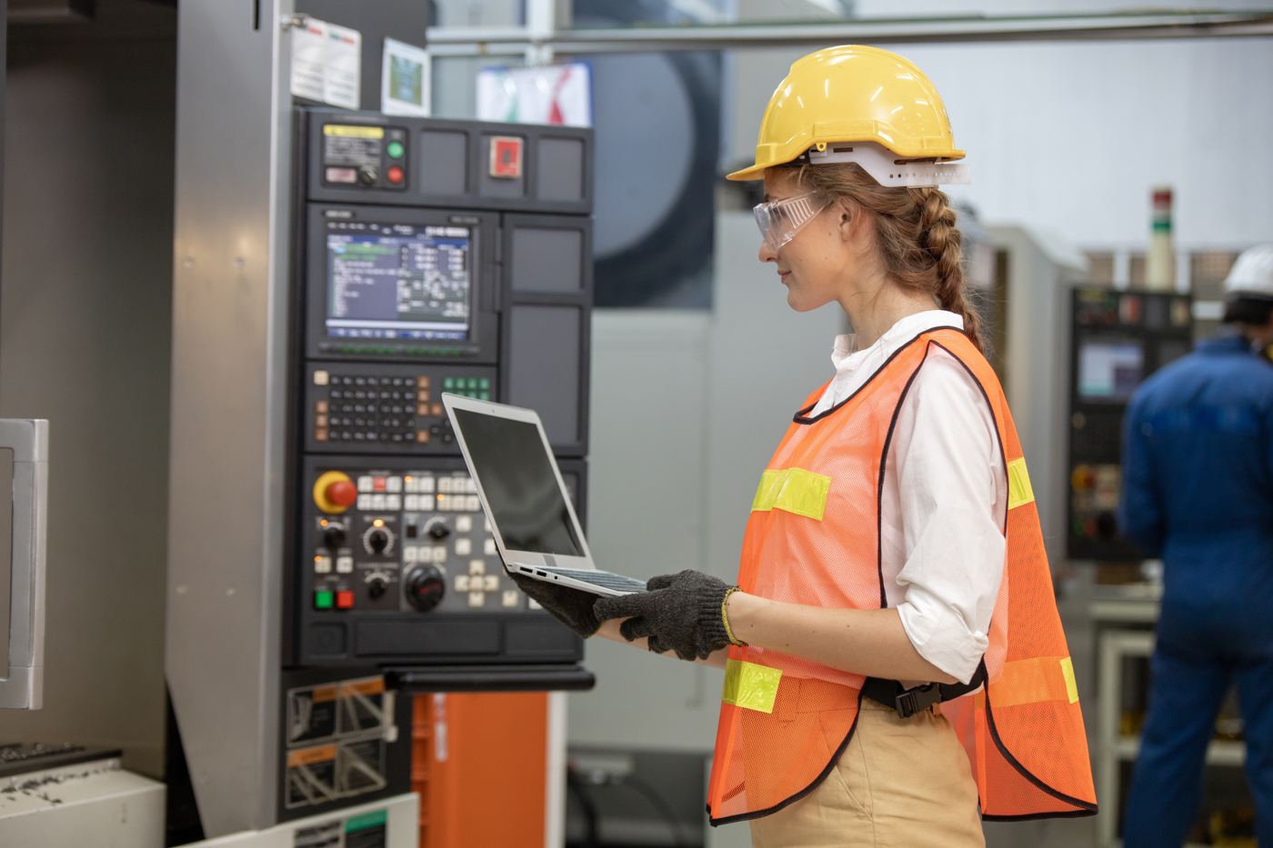 Factory floor worker in a hard hat reviewing data on a tablet