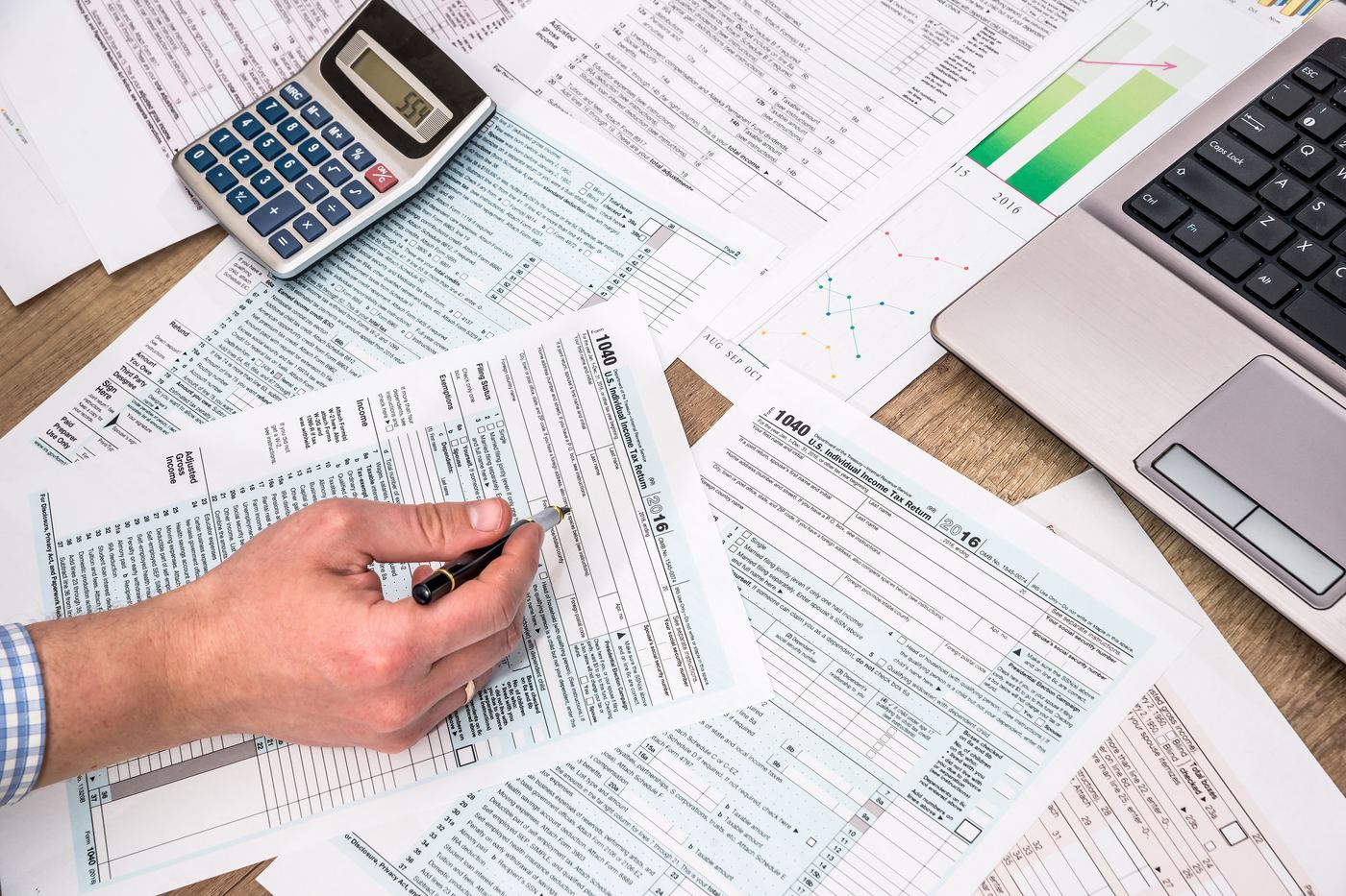 Tax and financial paperwork spread across a desk with a calculator and laptop